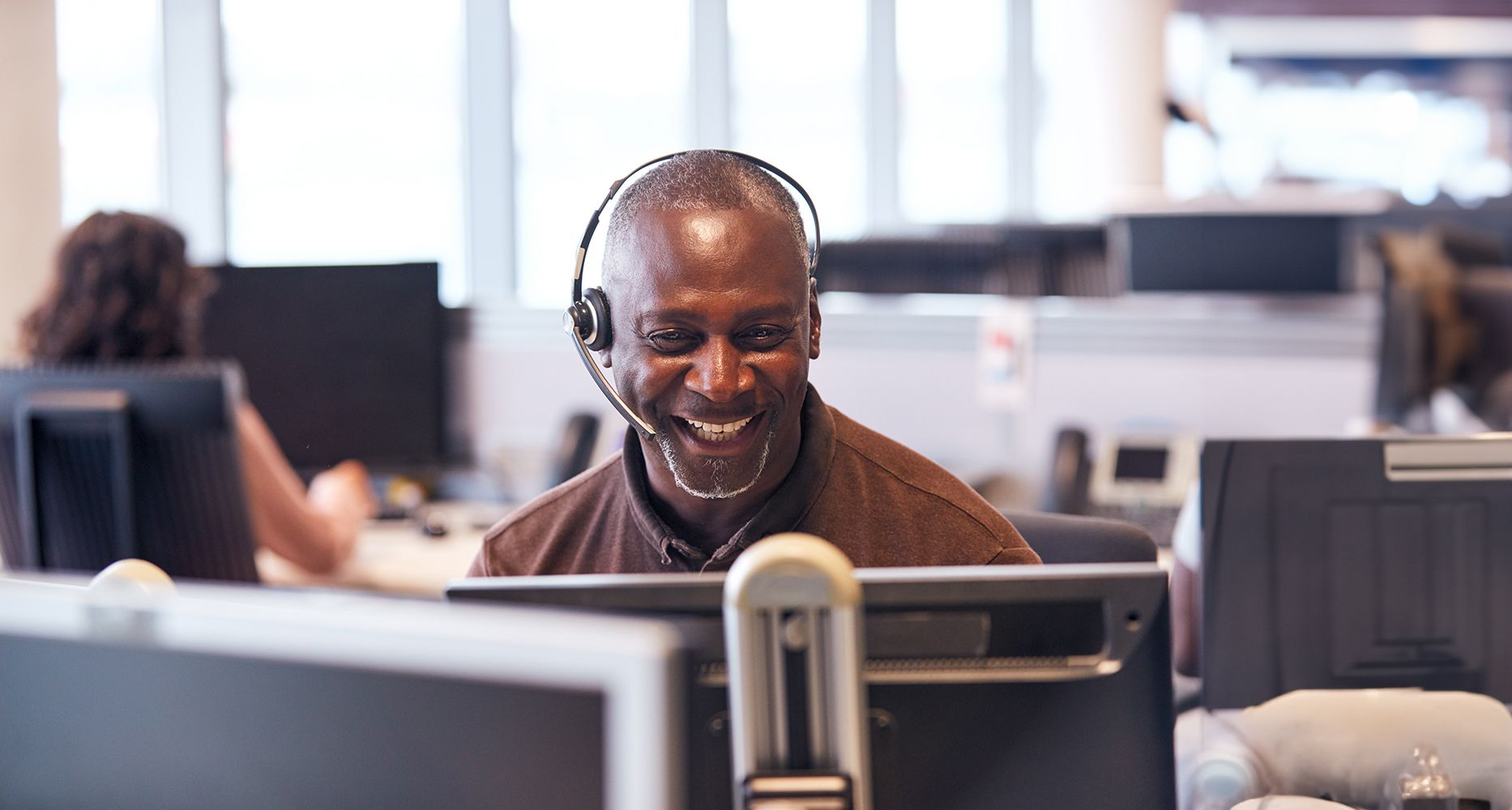 Mature Businessman Wearing Telephone Headset Talking To Caller In Customer Services Department